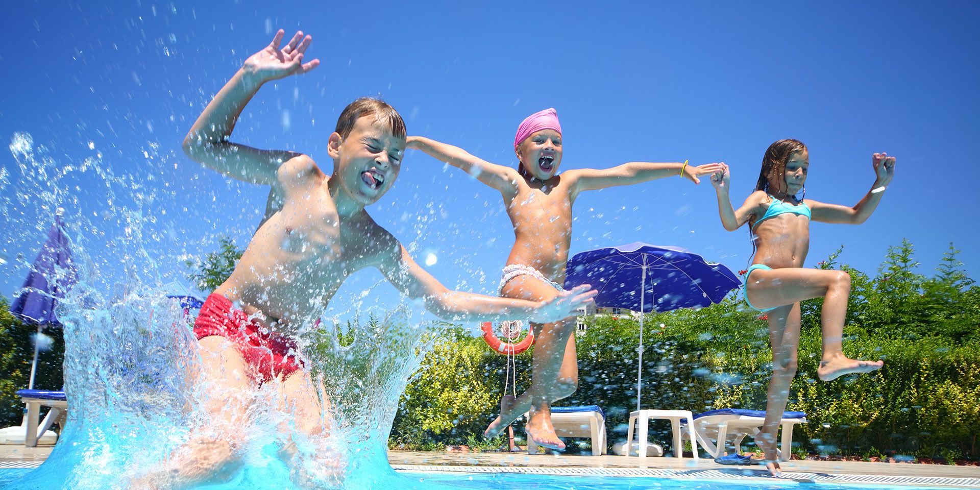 Drei Kinder springen fröhlich in einen Pool und genießen den Sommer.